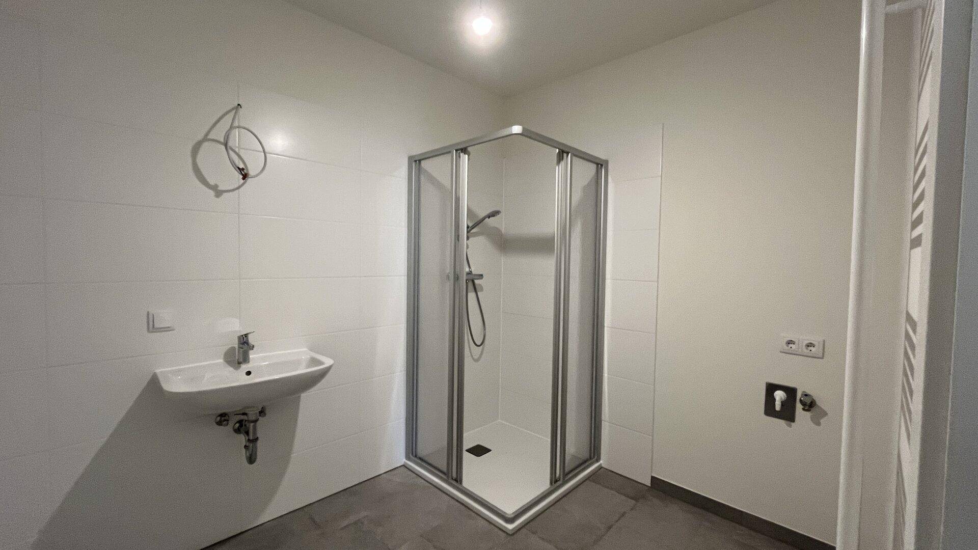 Modernes Badezimmer mit Duschkabine, Waschbecken, weißen Wandfliesen und grauem Boden.