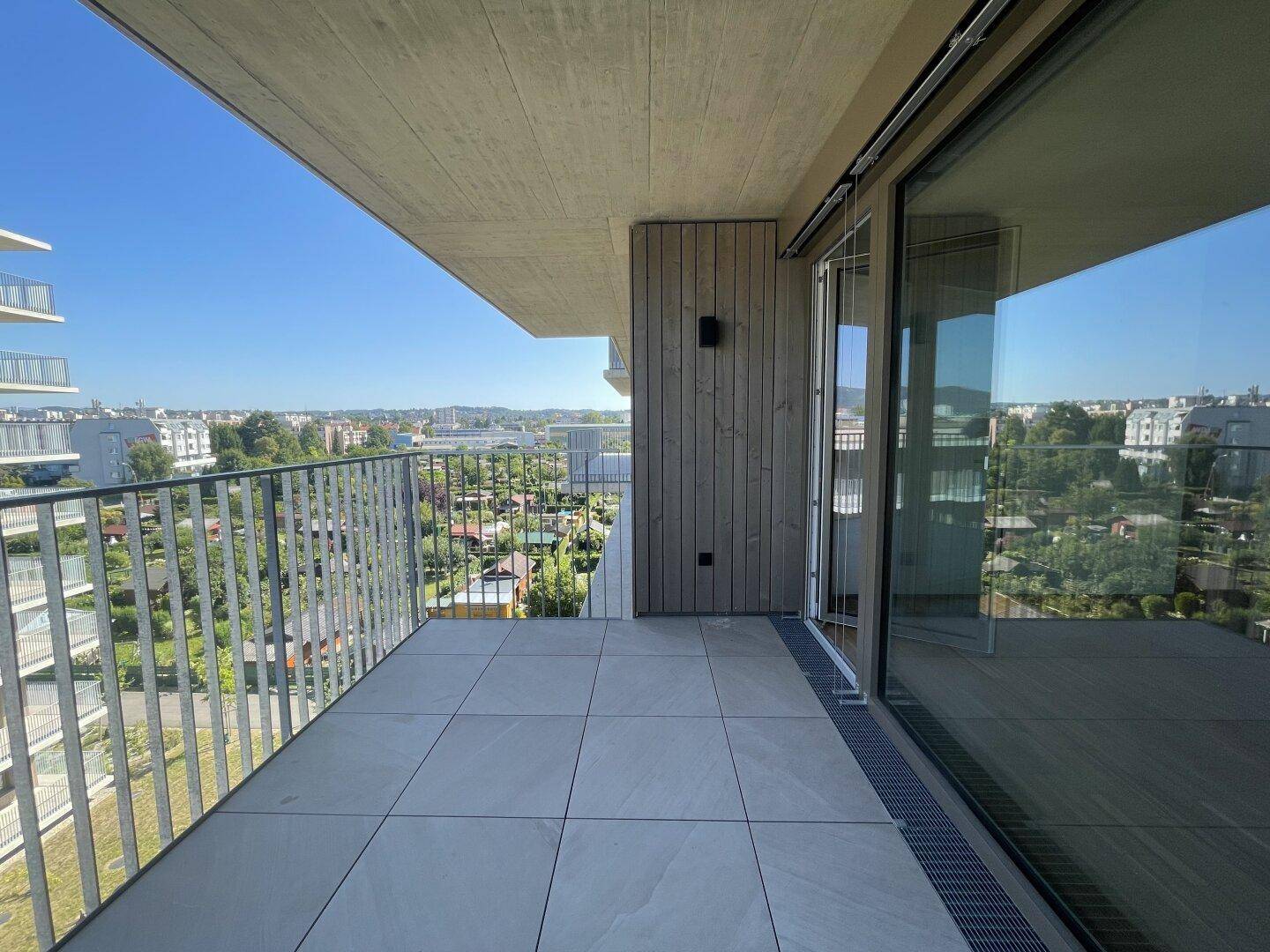 Heller Balkon mit moderner Fliesenoptik und Panoramablick auf die Stadt und grüne Flächen.