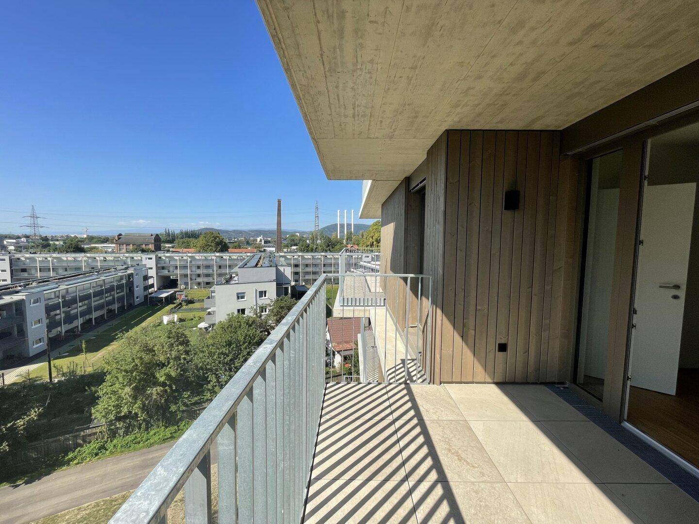 Geräumiger Balkon mit Holzverkleidung und Blick auf die umliegenden Gebäude und Grünflächen.