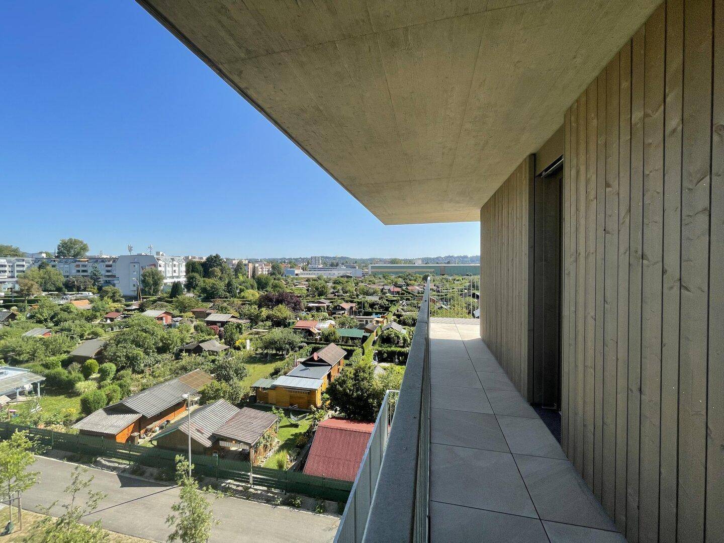 Geräumiger Balkon mit moderner Holzfassade und weitem Ausblick auf grüne Gärten.