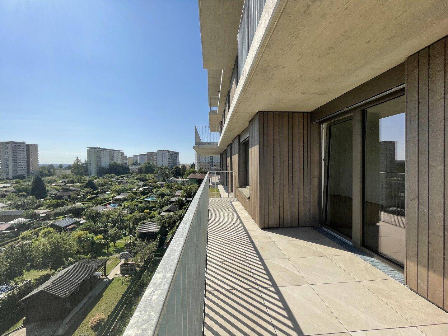 Langer Balkon mit Fliesenboden und Metallgeländer, bietet weiten Blick über Kleingärten.