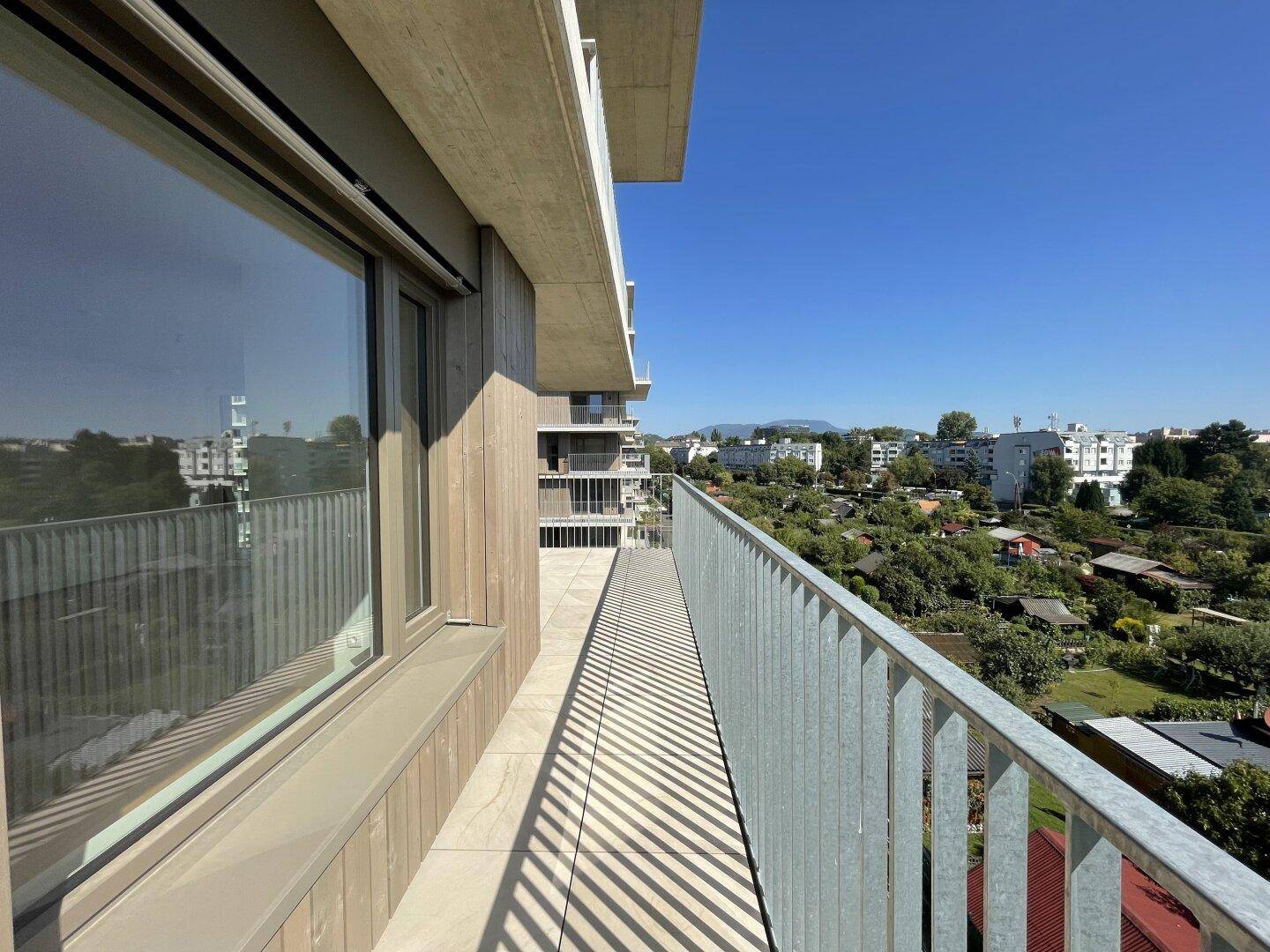 Heller Balkon entlang der Fassade mit großen Fenstern und Blick auf die Umgebung.