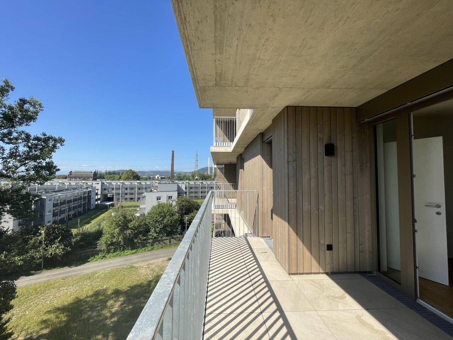 Moderner Balkon mit Holzfassade und Blick auf die Umgebung sowie weitere Gebäude.