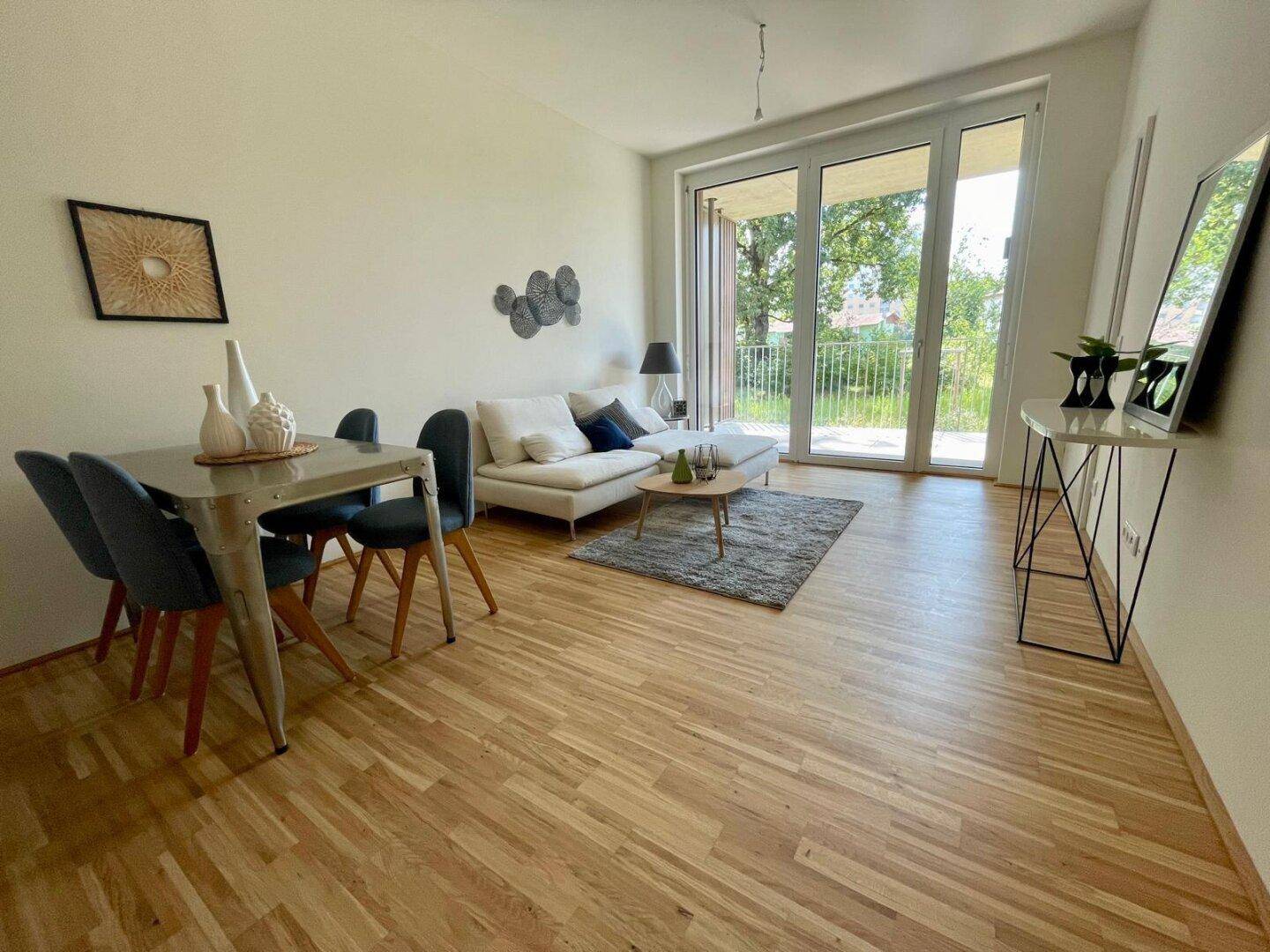 Offener Wohn-Essbereich mit hellem Holzparkett und Zugang zu einem sonnigen Balkon.