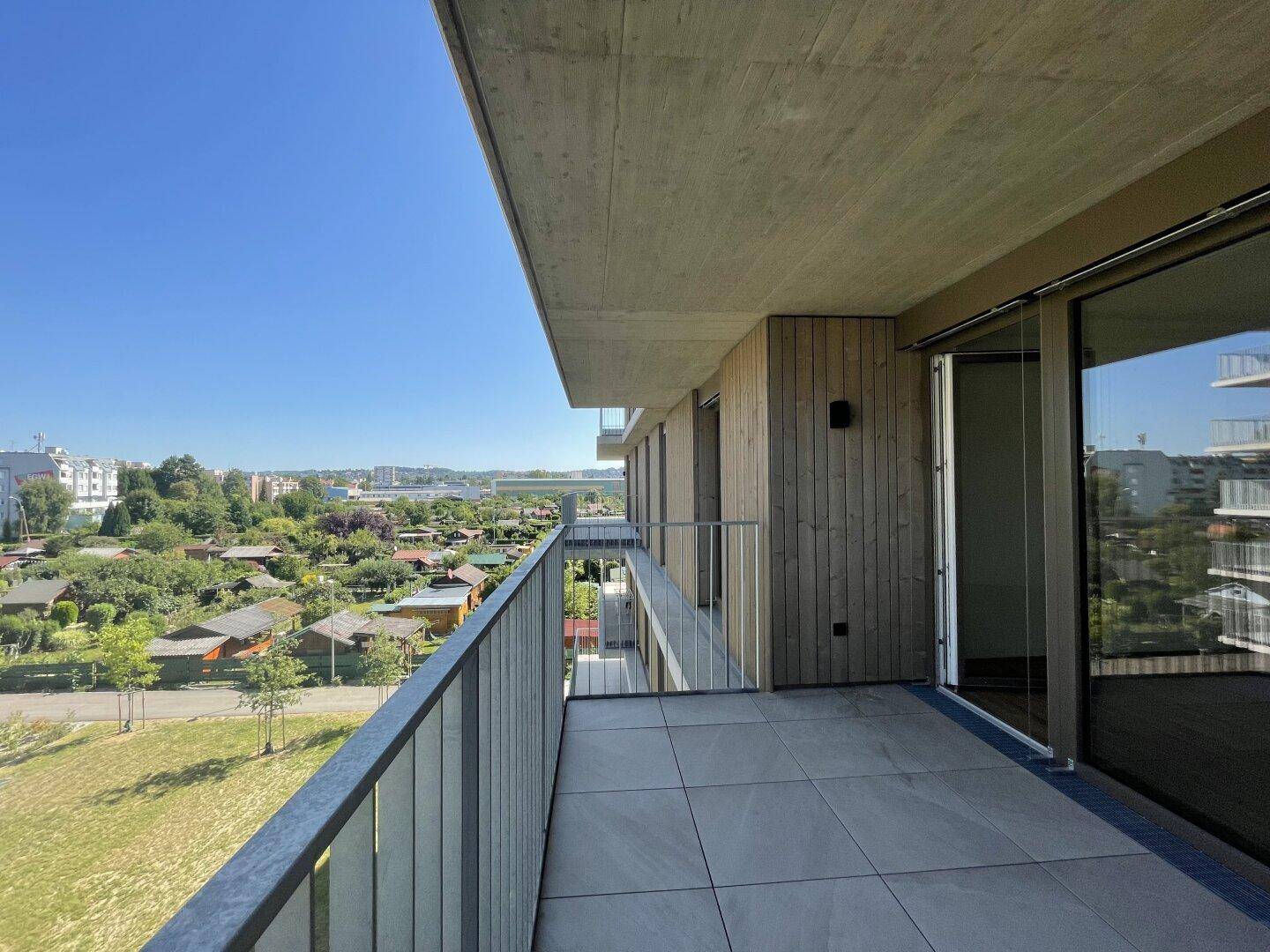 Sonniger Balkon mit Fliesenboden und weitem Blick über grüne Gärten und die Umgebung.