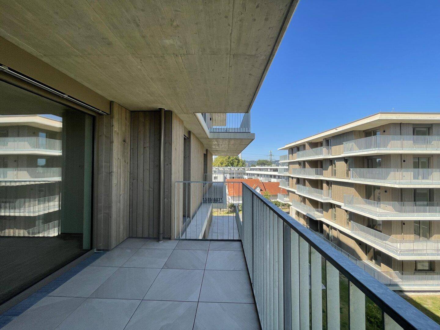 Balkon mit Fliesenboden und Holzverkleidung, bietet einen Blick auf die moderne Architektur der Nachbargebäude.