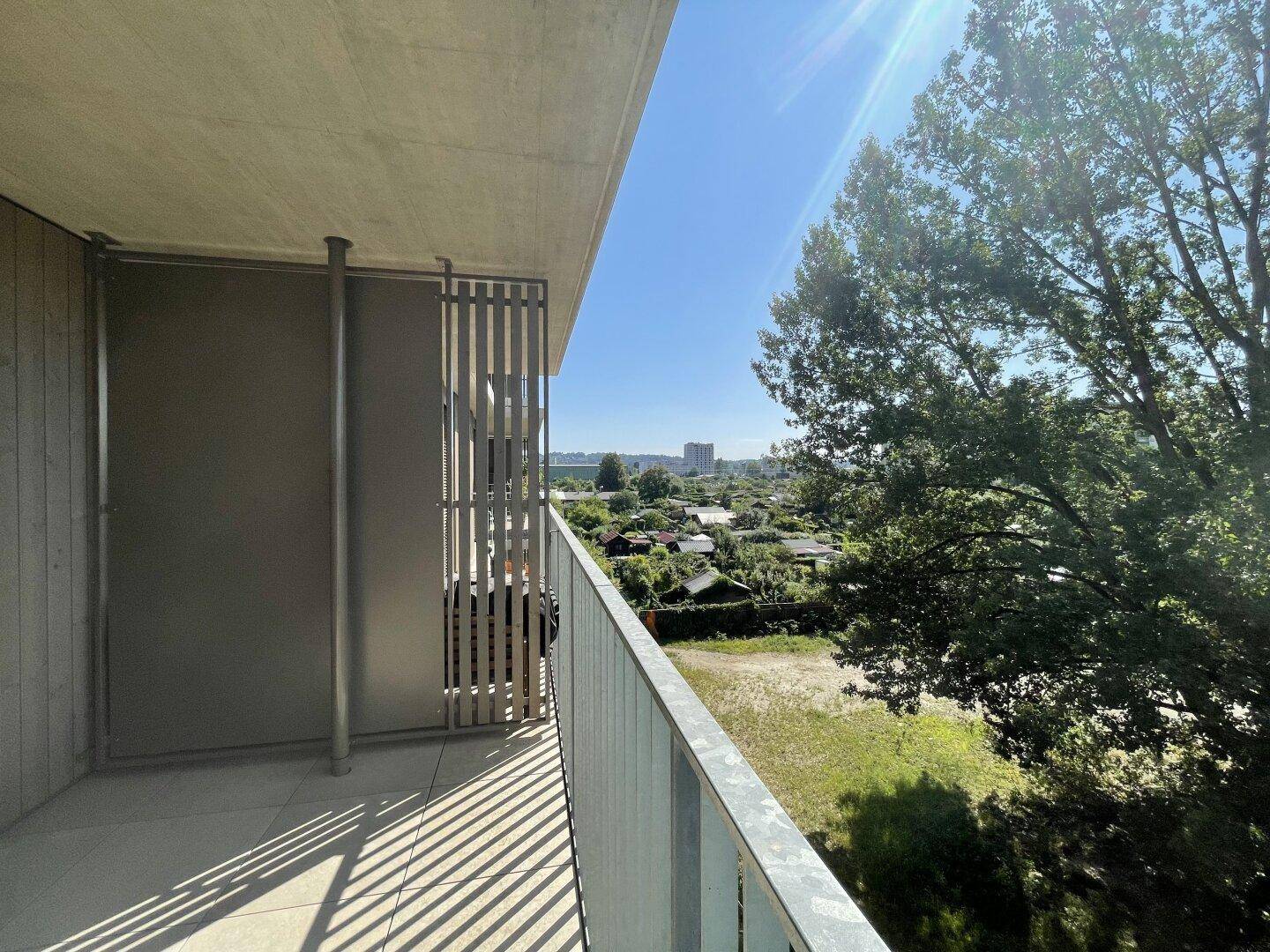 Heller Balkon mit Blick auf die grüne Umgebung und weitere Gebäude.
