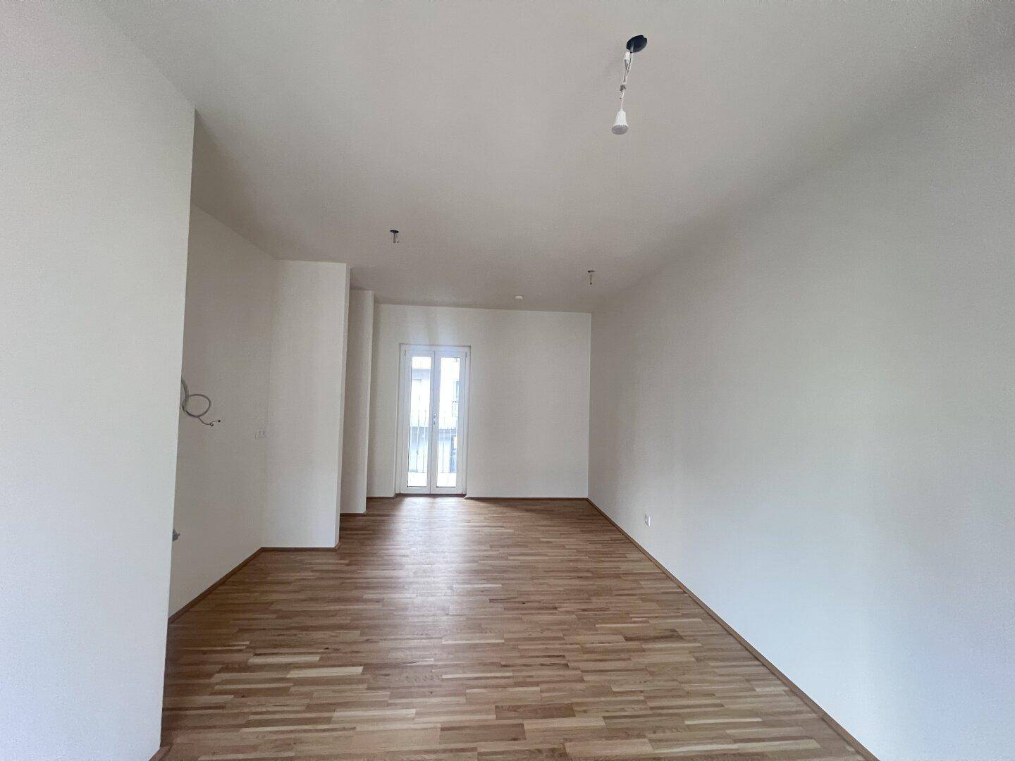 Geräumiger, heller Wohnbereich mit Parkettboden und Zugang zu einem Balkon oder einer Terrasse.