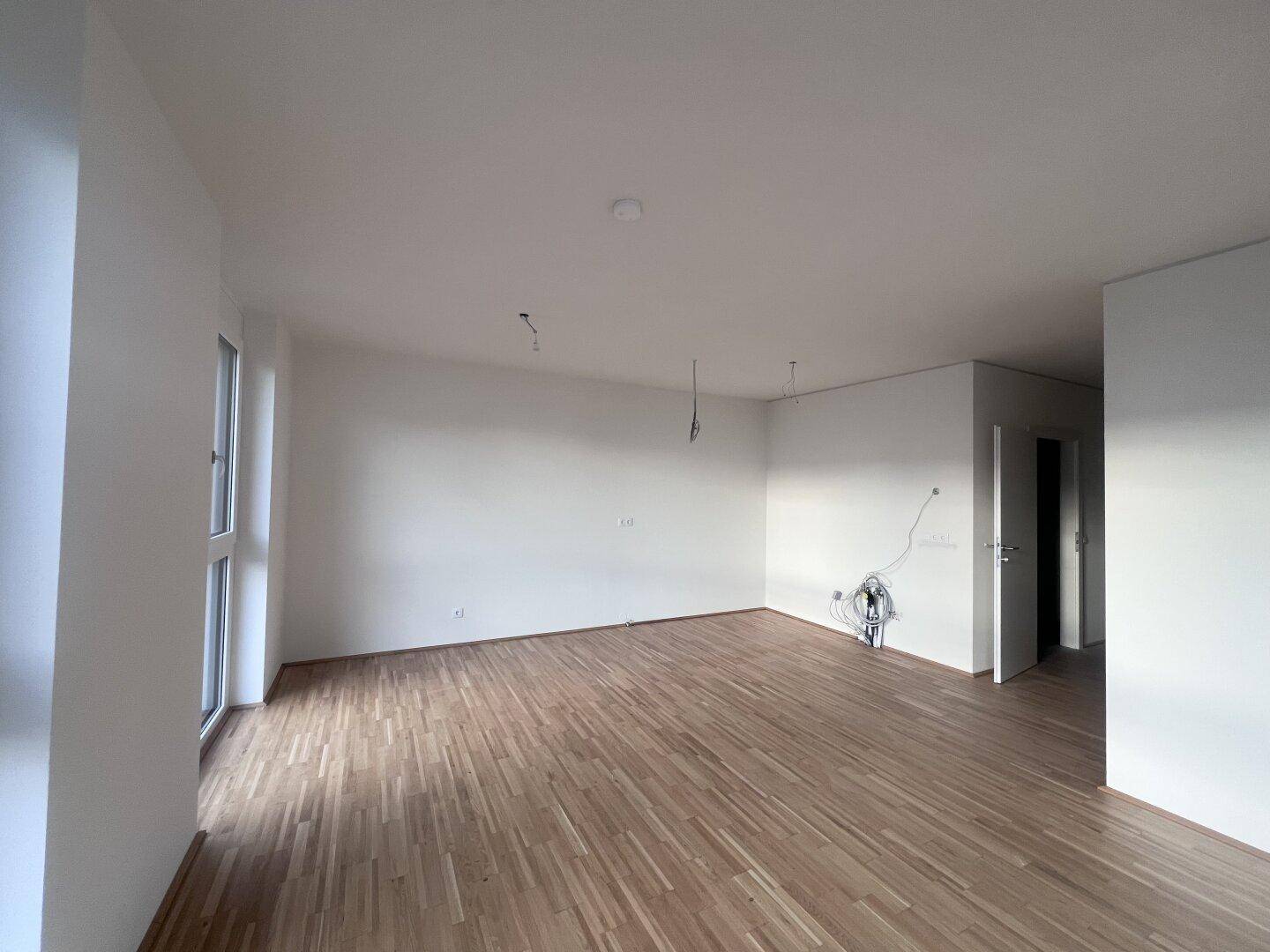 Heller, unmöblierter Wohnbereich mit Parkettboden und großen Fenstern in einem Neubau.