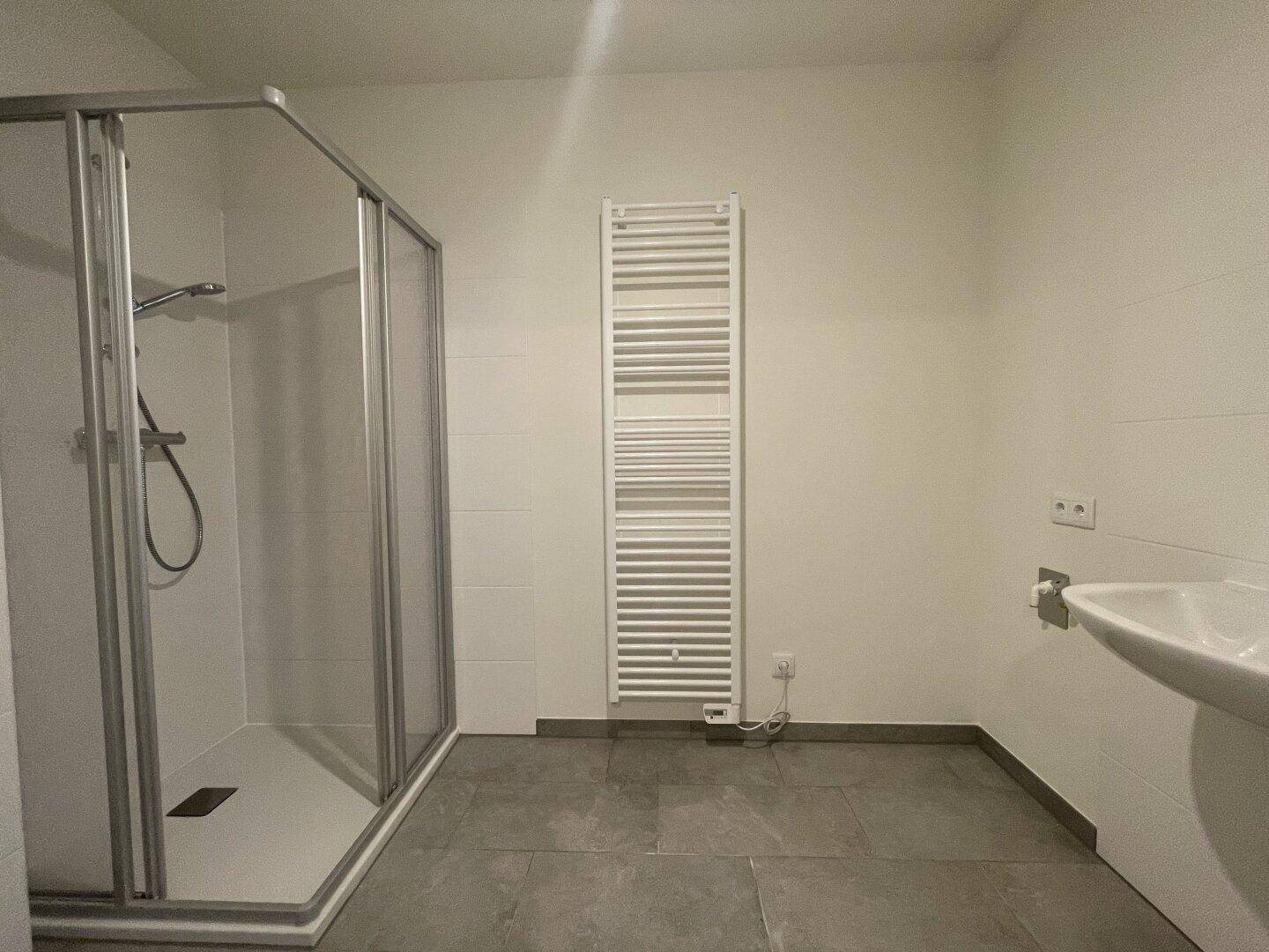 Modernes Badezimmer mit Duschkabine, beheiztem Handtuchhalter und grauem Fliesenboden.