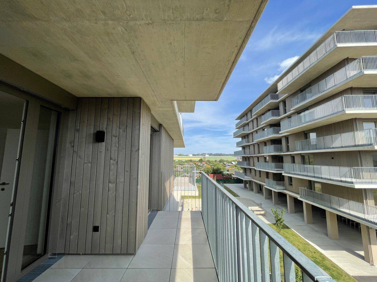 Balkon mit Blick auf die moderne Architektur der Wohnanlage und die grüne Umgebung.