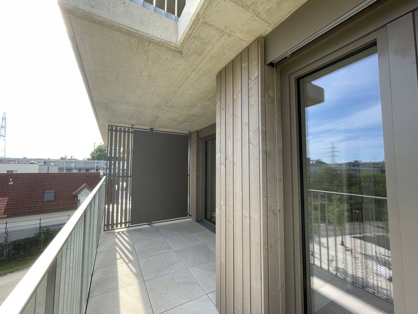Moderner Balkon mit Fliesenboden und Holzverkleidung, der einen weiten Blick auf die Umgebung bietet.