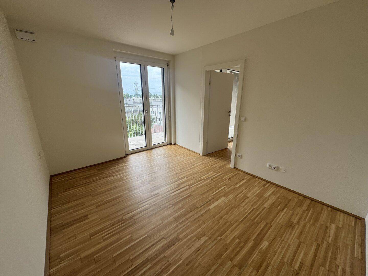 Lichtdurchfluteter Raum mit Parkettboden und Zugang zu einem Balkon, ideal für verschiedene Nutzungen.
