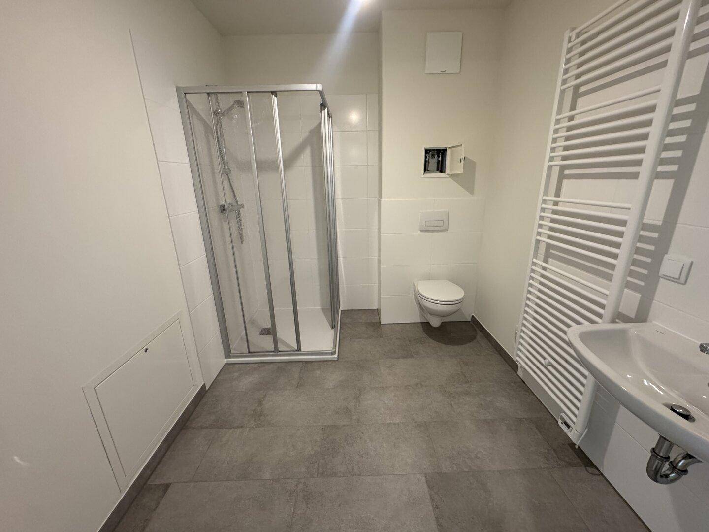 Modernes Badezimmer mit Dusche, WC, Waschbecken und beheiztem Handtuchhalter in hellen Farben.