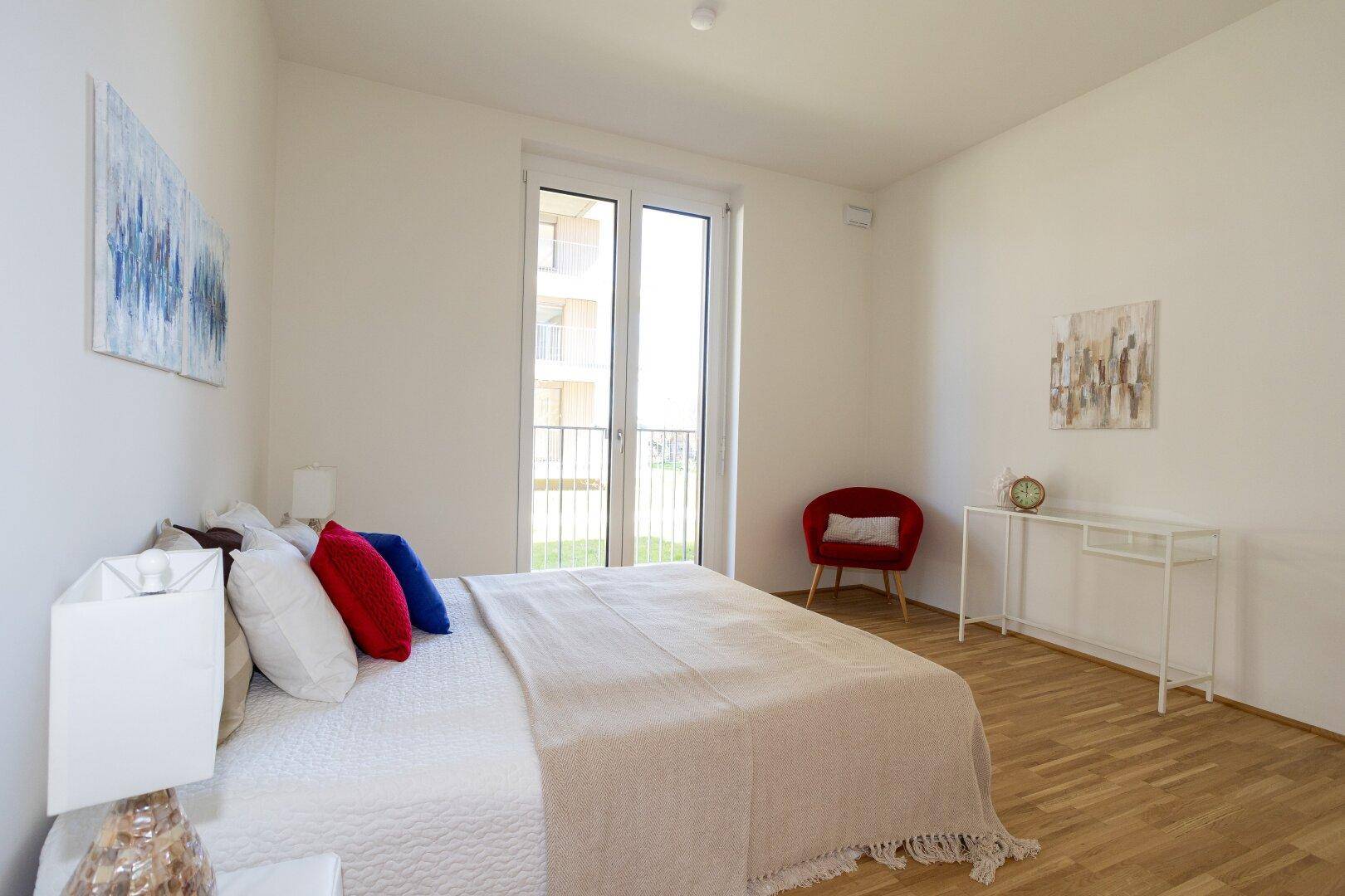 Helles Schlafzimmer mit Doppelbett, Holzboden und Zugang zu einem Balkon oder Garten.