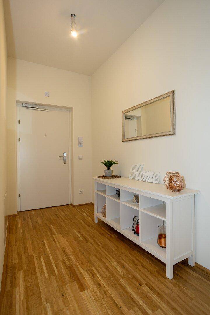 Heller Eingangsbereich mit Holzboden, weißem Regal und einem Spiegel an der Wand.