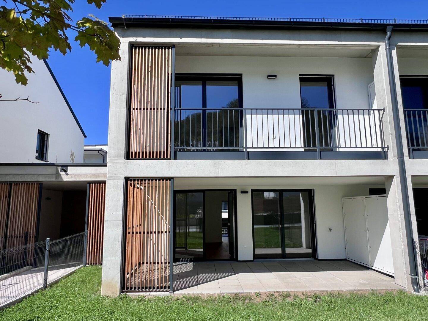 Moderne Gebäudefassade eines Neubaus mit Balkon und Terrasse im Erdgeschoss.
