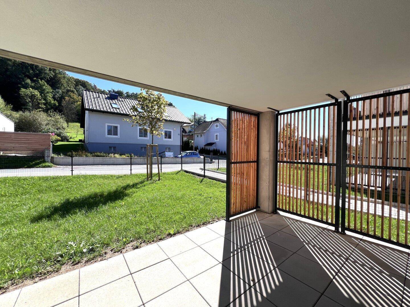 Geräumige überdachte Terrasse mit Fliesenboden und Blick auf die grüne Umgebung.