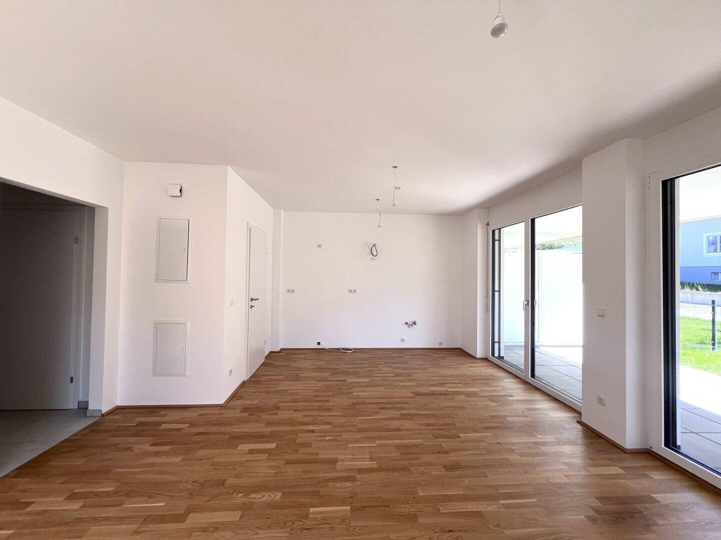 Heller, leerer Wohnraum mit Eichenparkett und großen Schiebetüren zur Terrasse.