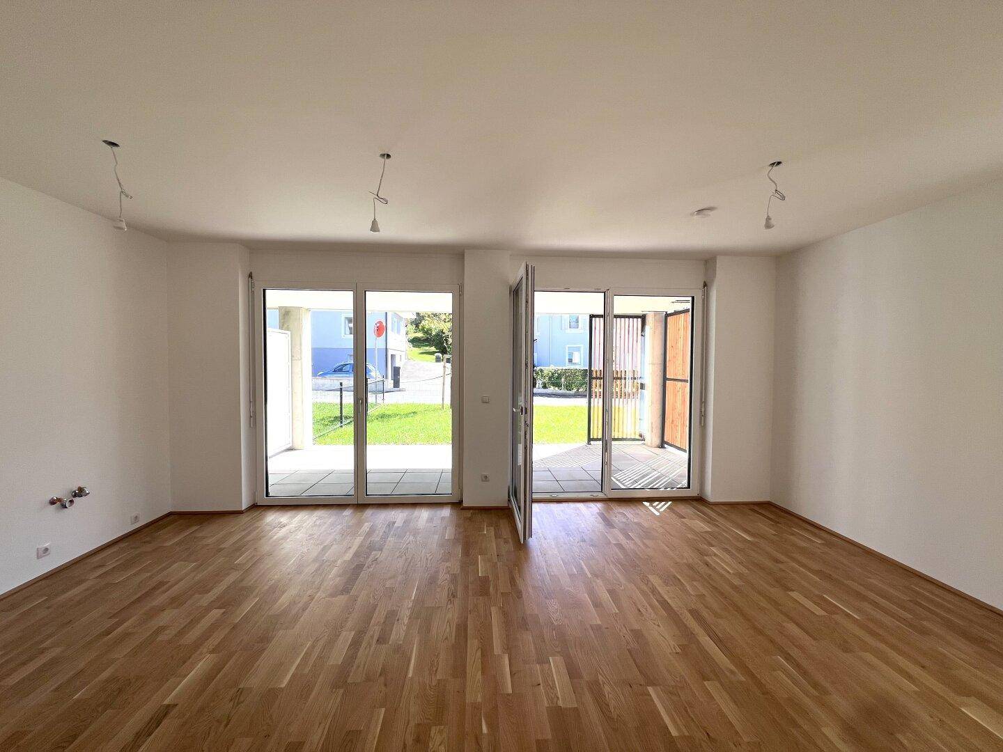 Lichtdurchfluteter Wohnbereich mit Holzboden und direktem Zugang zu zwei Außenterrassen.