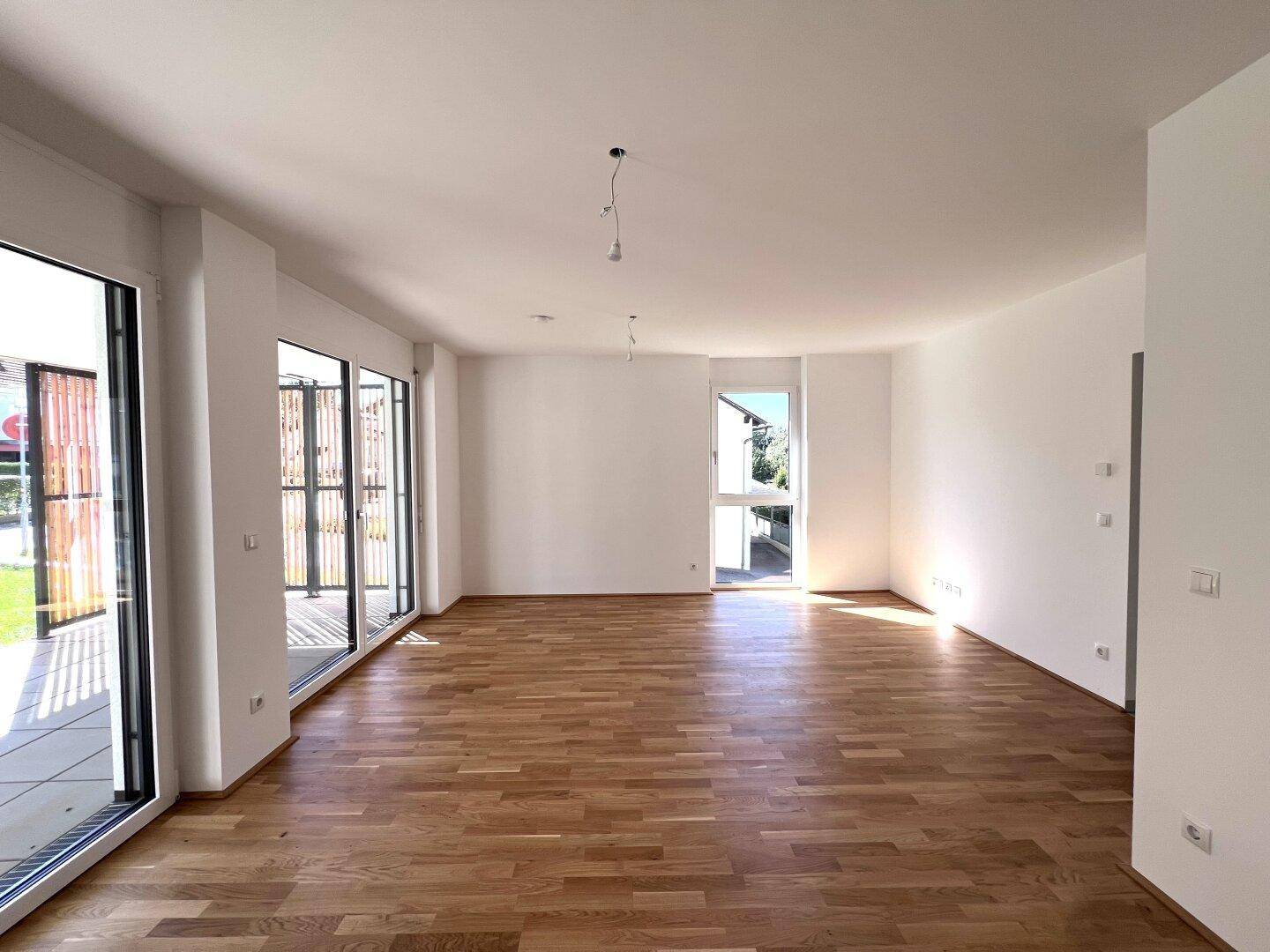 Geräumiger, heller Wohnraum mit Parkettboden und großen Fenstern mit Sichtschutz.