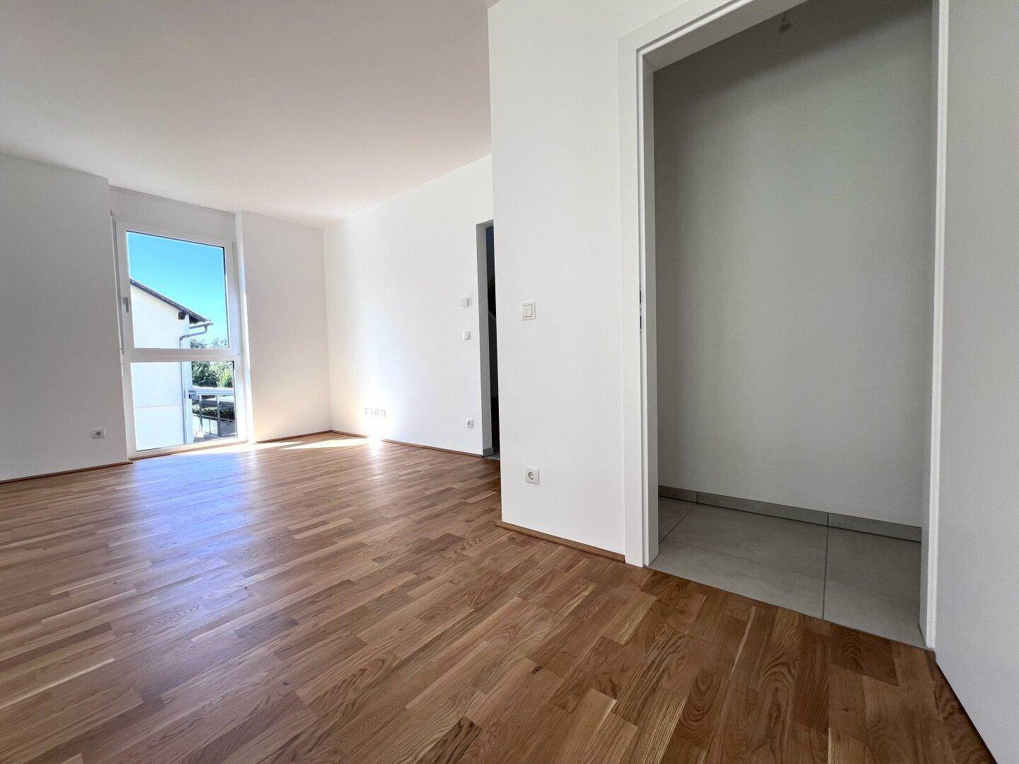 Heller Raum mit Parkettboden und offenem Zugang zu einem gefliesten Abstellbereich.