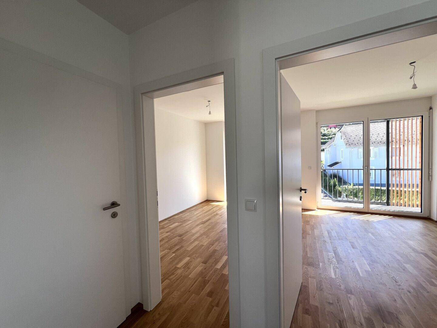 Flur mit Zugang zu mehreren hellen Räumen, darunter ein Zimmer mit Balkonzugang.