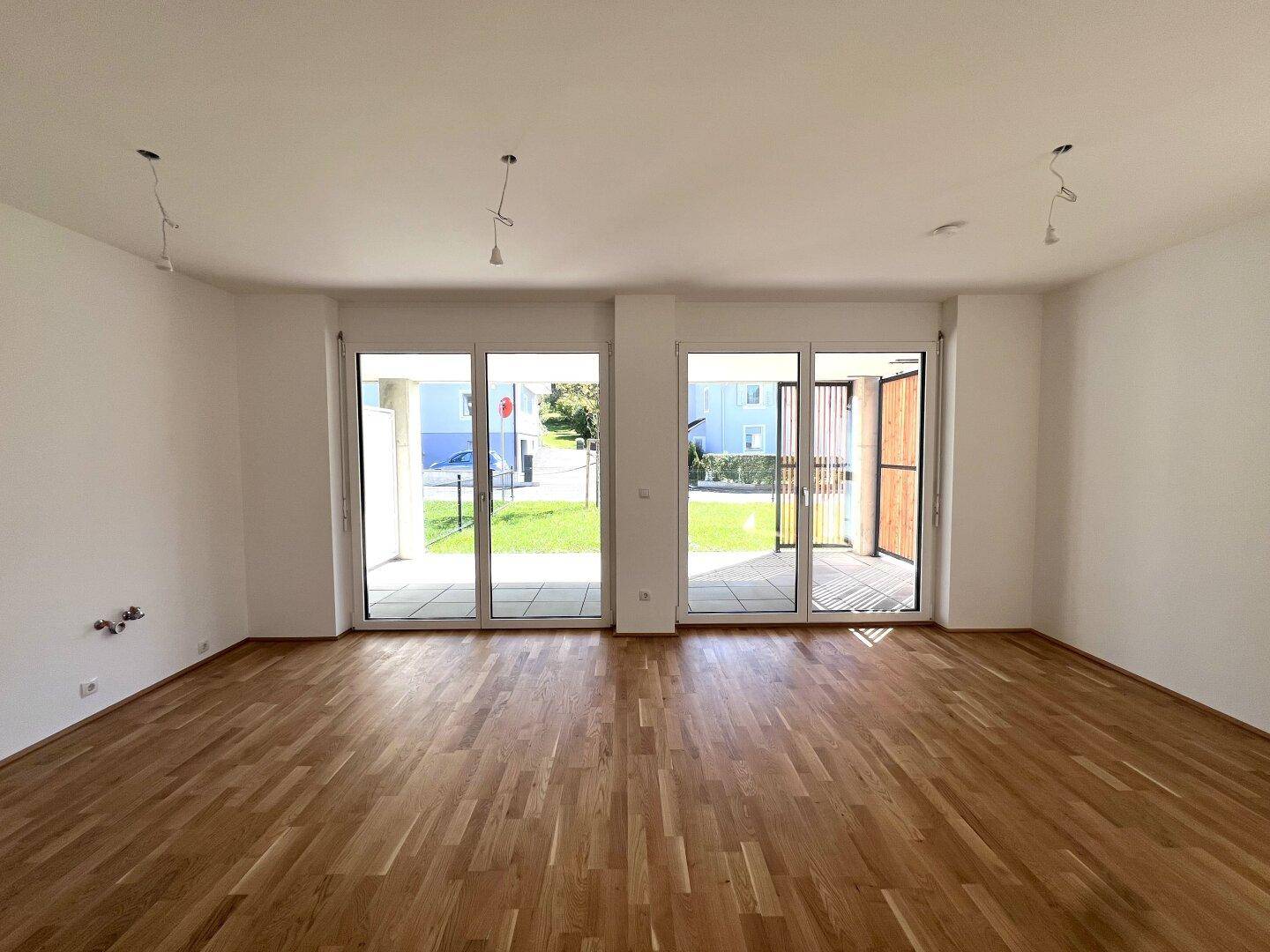 Geräumiger Wohnbereich mit Holzboden und großen Glasfronten, die viel Licht spenden.
