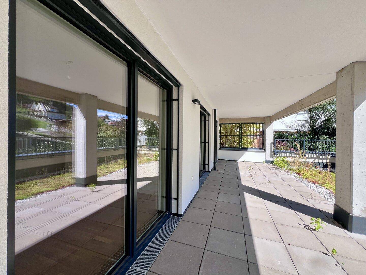 Detailansicht der gefliesten Terrasse mit großen Glasschiebetüren und angrenzender Grünfläche.