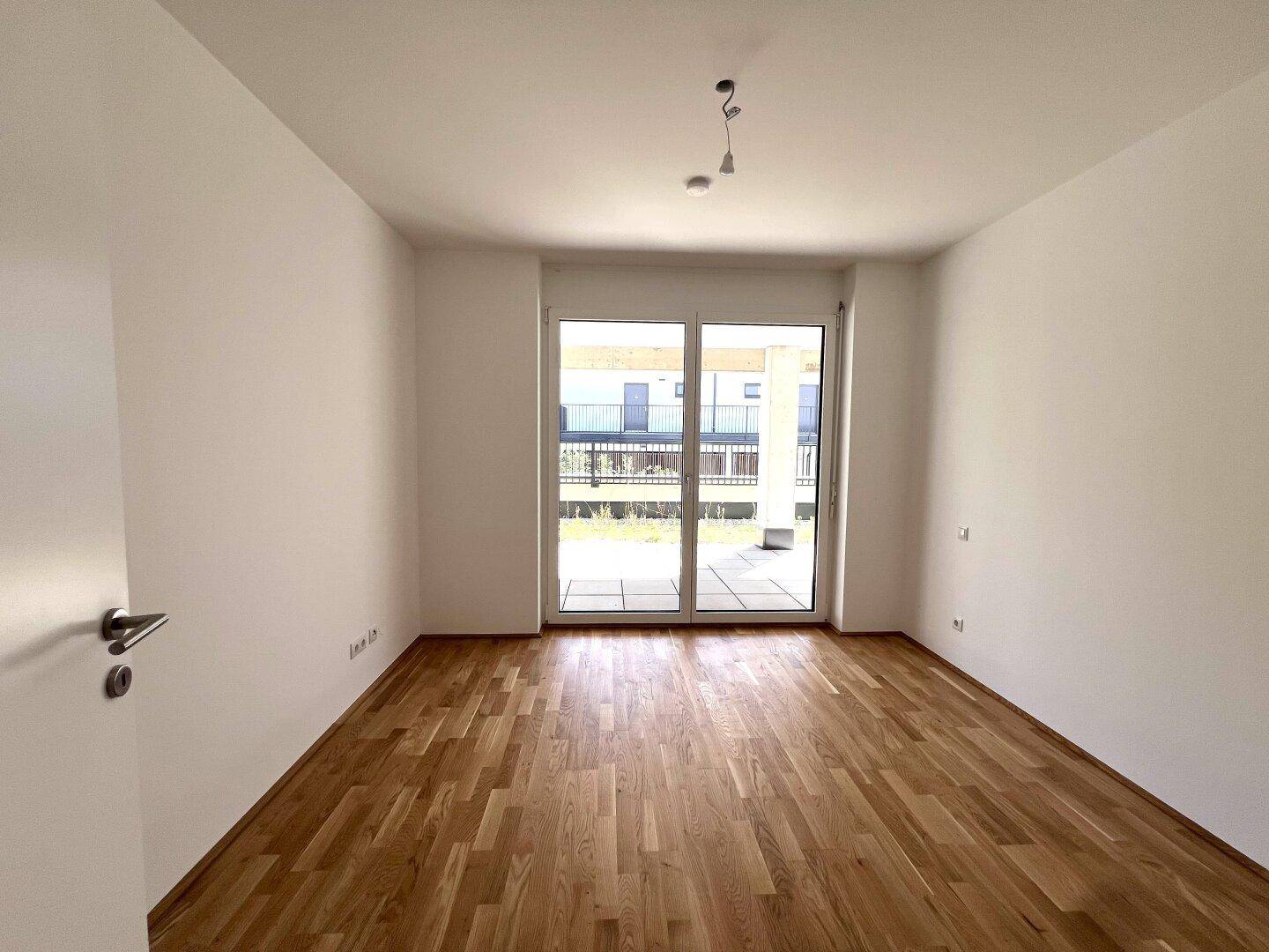 Schlafzimmer mit Parkettboden und direktem Zugang zu einer Terrasse durch eine große Schiebetür.