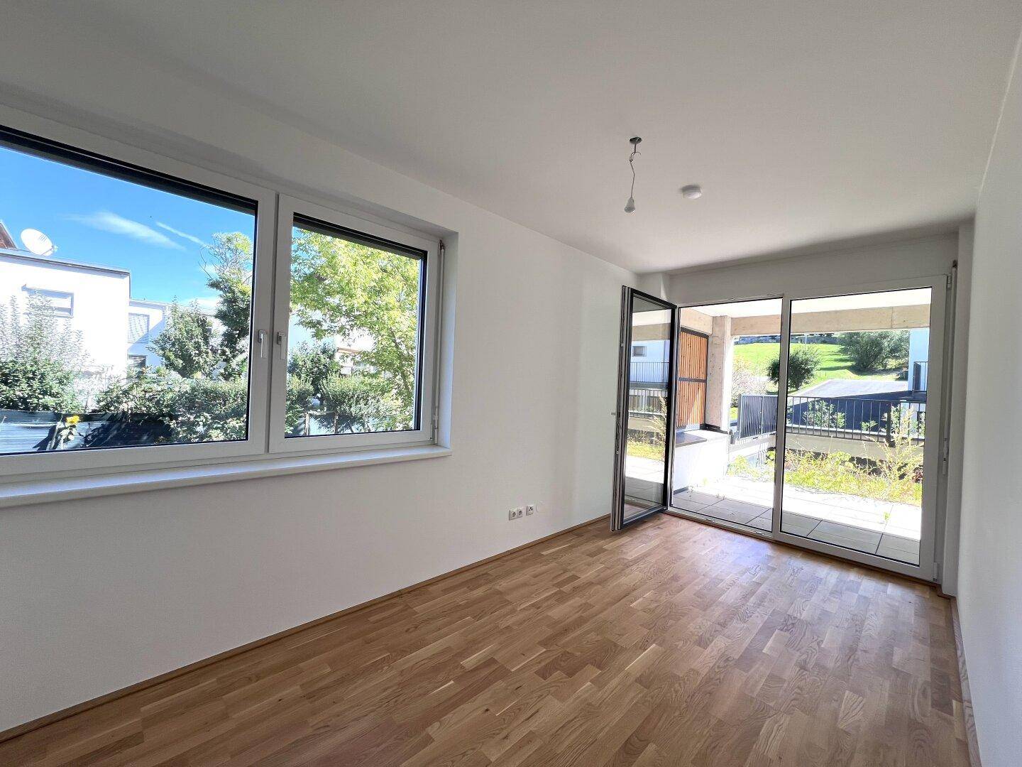 Geräumiges Wohnzimmer mit Parkettboden, großen Fenstern und direktem Zugang zur Terrasse.
