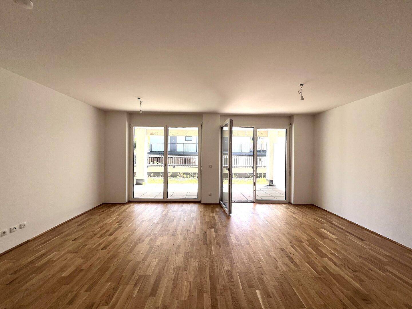 Großes, helles Wohnzimmer mit Parkettboden und zwei Zugängen zu den Außenbereichen.