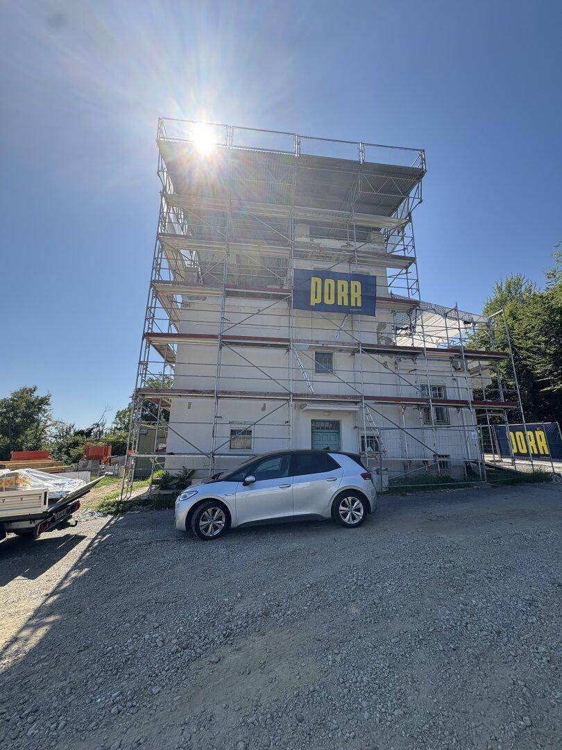 Gebäude im Bau mit Gerüsten und einem geparkten Auto unter strahlendem Sonnenschein.