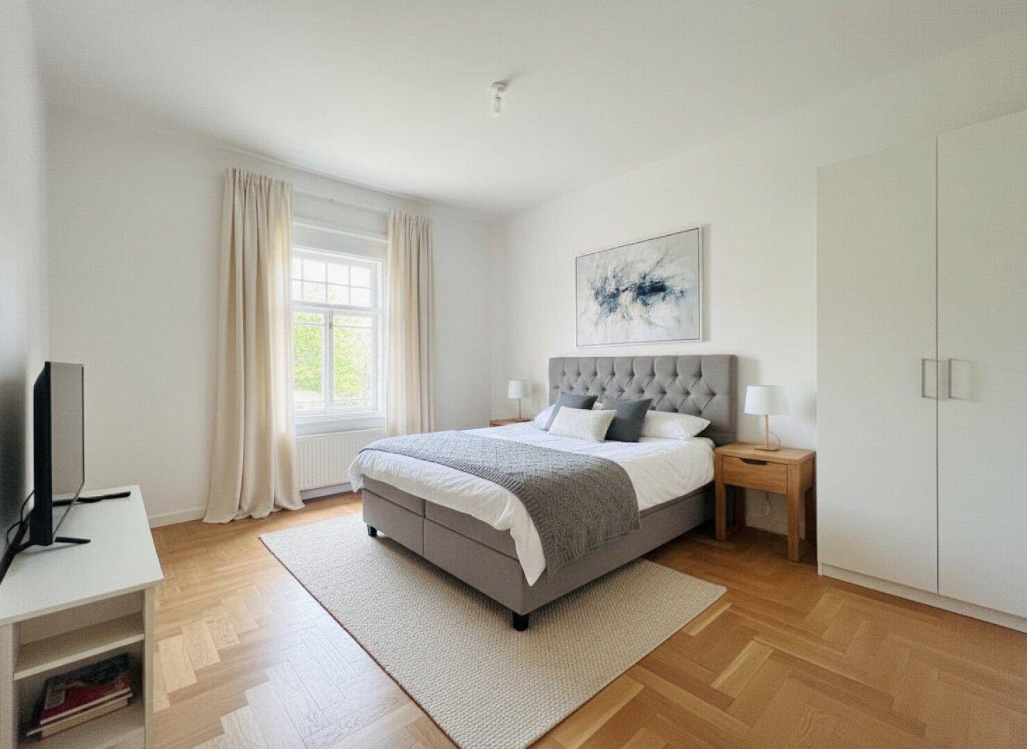 Helles Schlafzimmer mit Doppelbett, Parkettboden und weißen Einbauschränken.