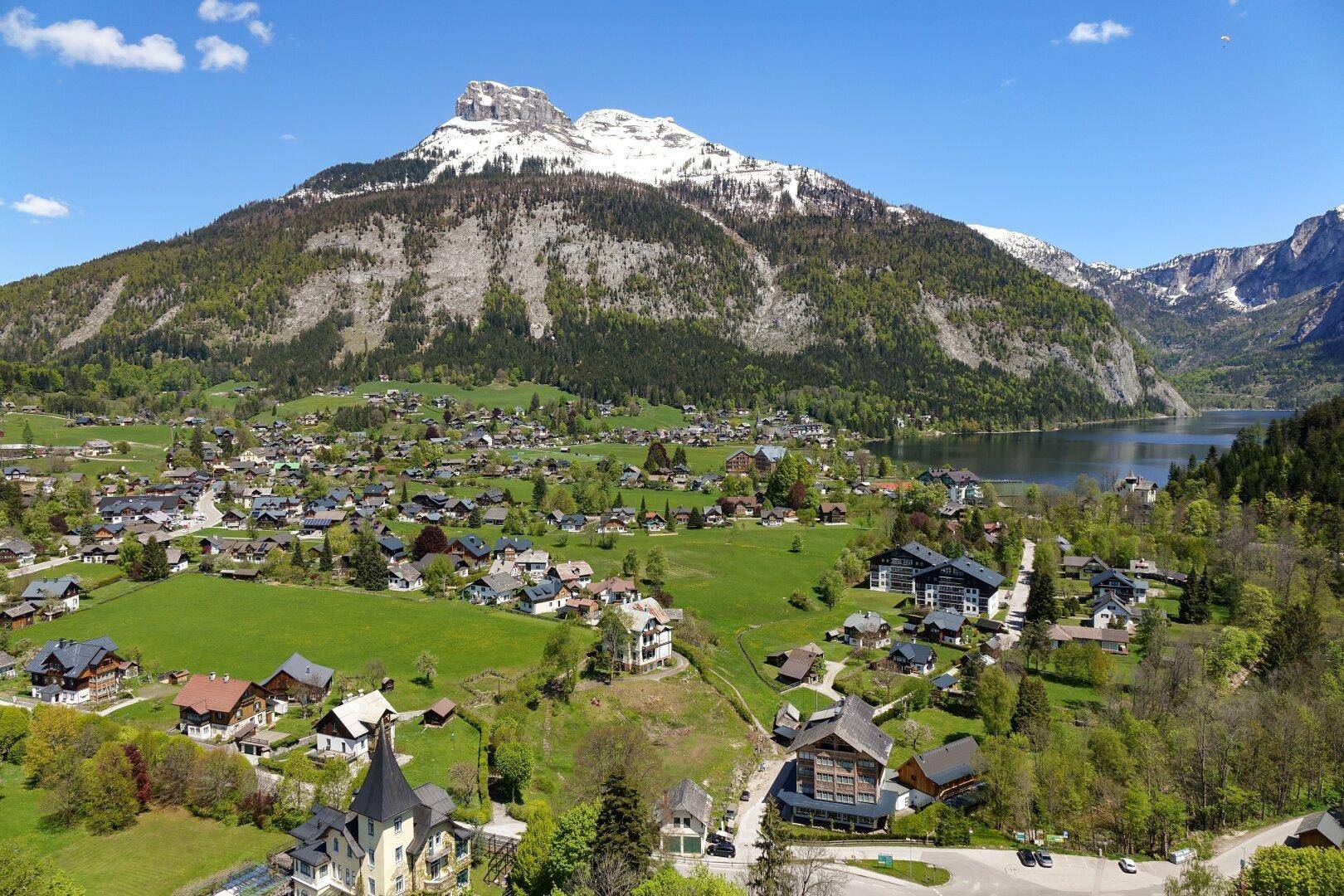 Panoramablick auf ein malerisches Dorf am Seeufer, umgeben von majestätischen Bergen und grünen Hügeln.