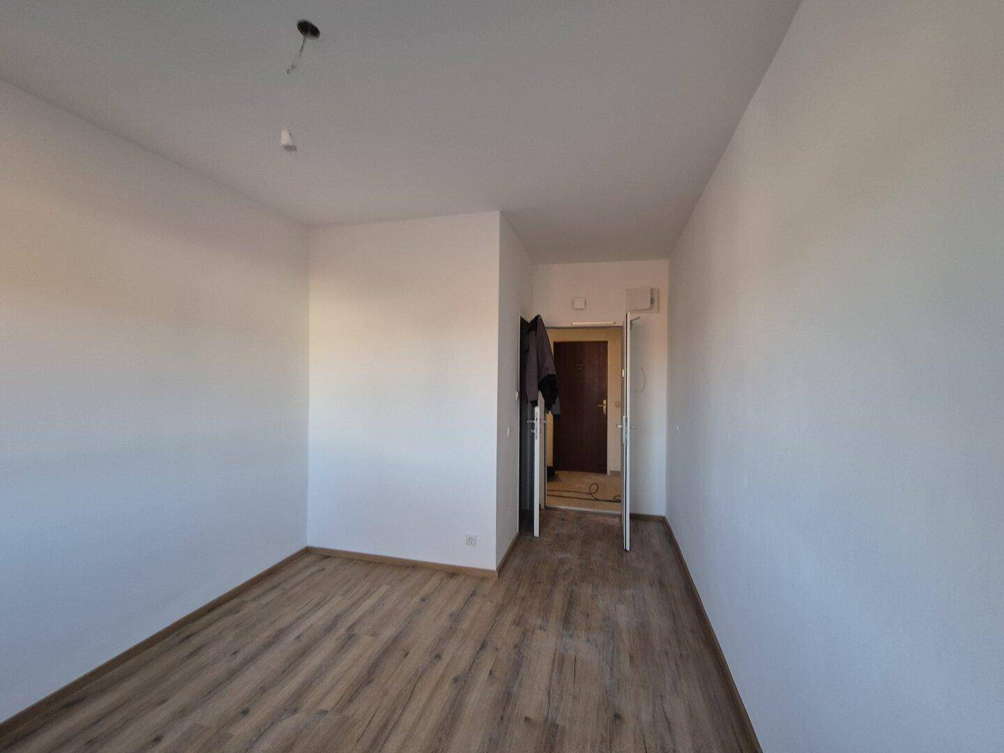 Heller Wohnbereich mit Laminatboden und Zugang zu einem weiteren Raum durch eine offene Tür.