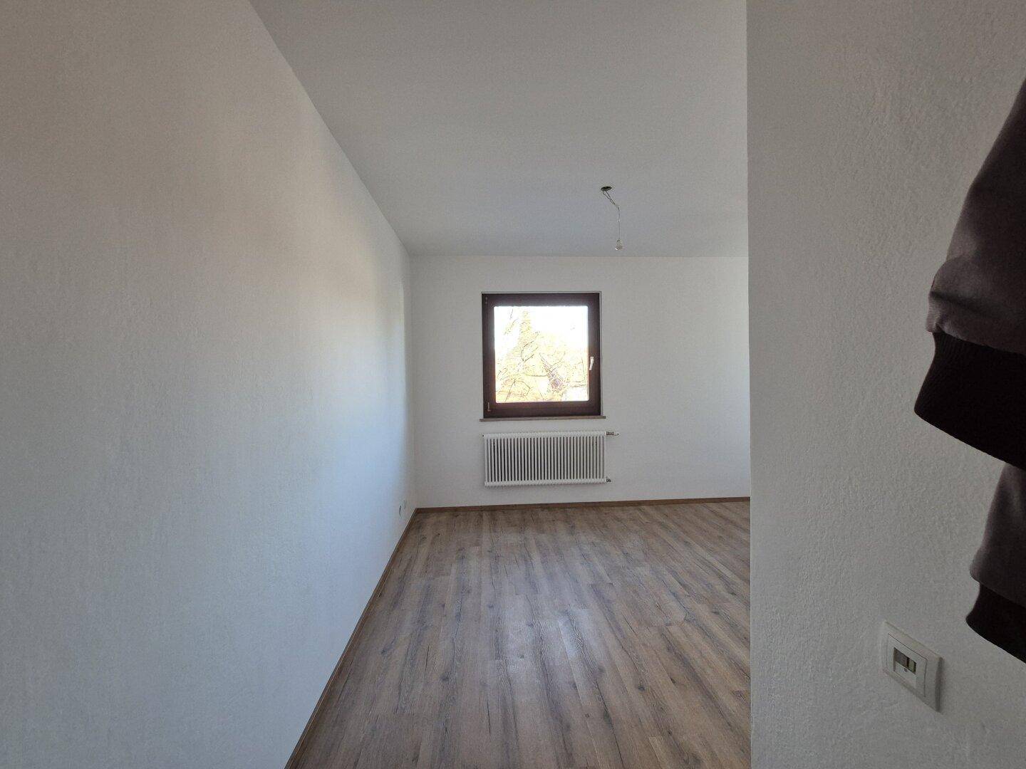 Geräumiger, heller Wohnraum mit Laminatboden, Fenster und Heizkörper unter dem Fenster.