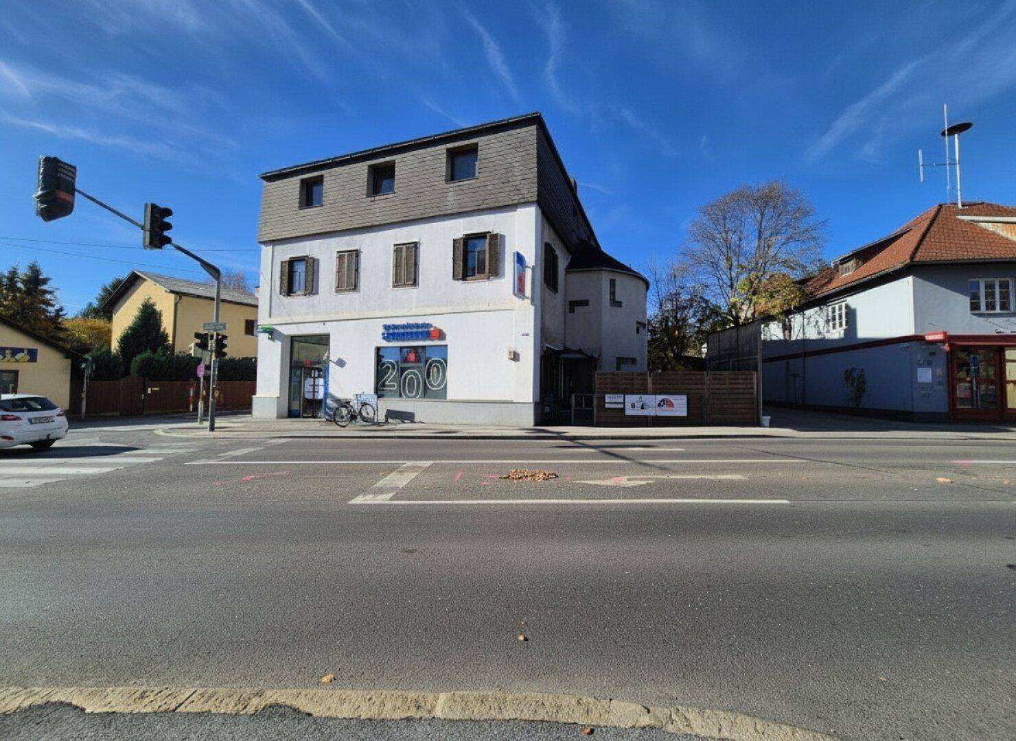 Eckgebäude an einer belebten Kreuzung mit Geschäften und Wohnungen unter blauem Himmel.