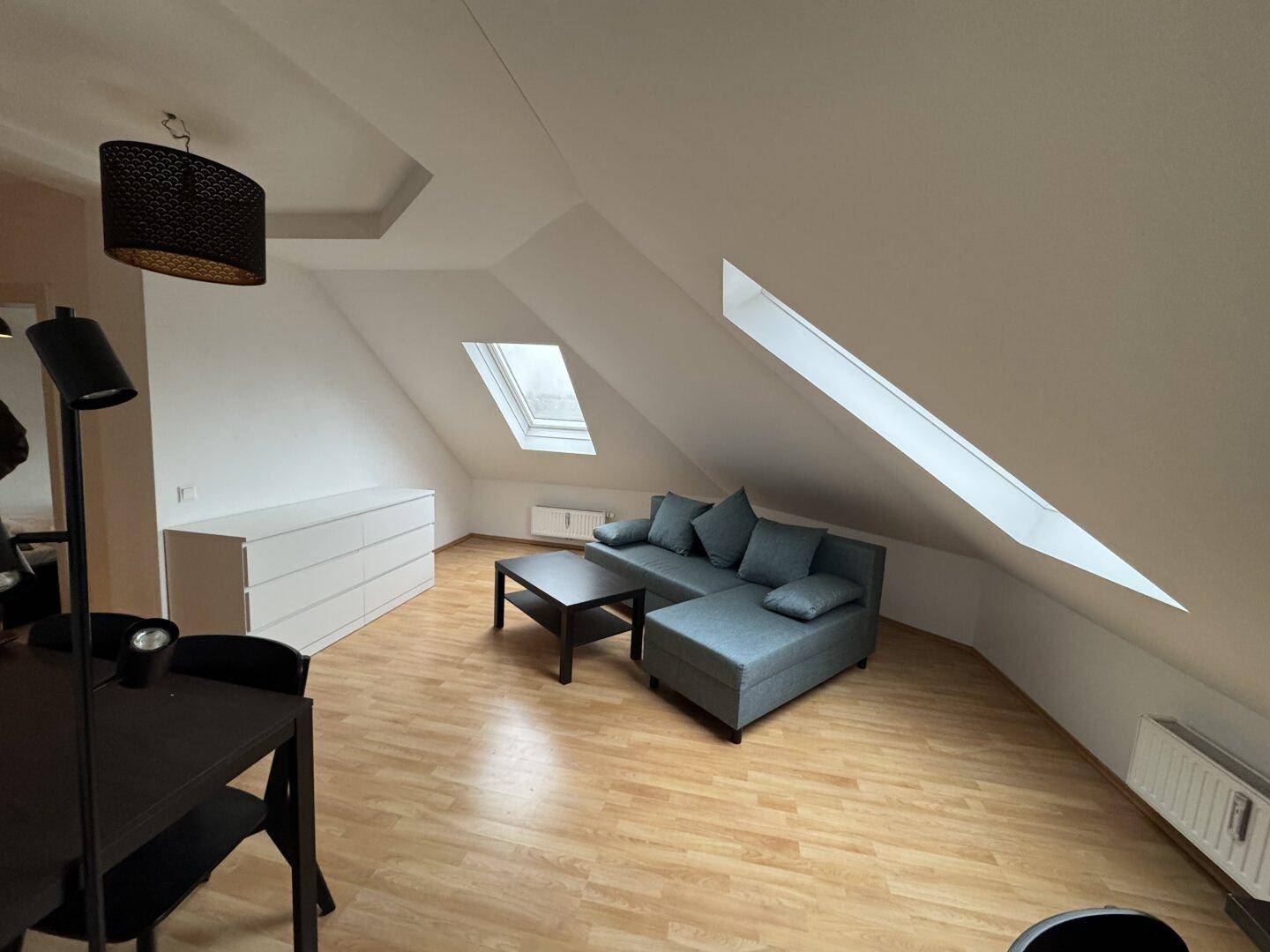 Gemütlicher Wohnbereich im Dachgeschoss mit Sofa, Couchtisch und schrägen Dachfenstern für viel Licht.