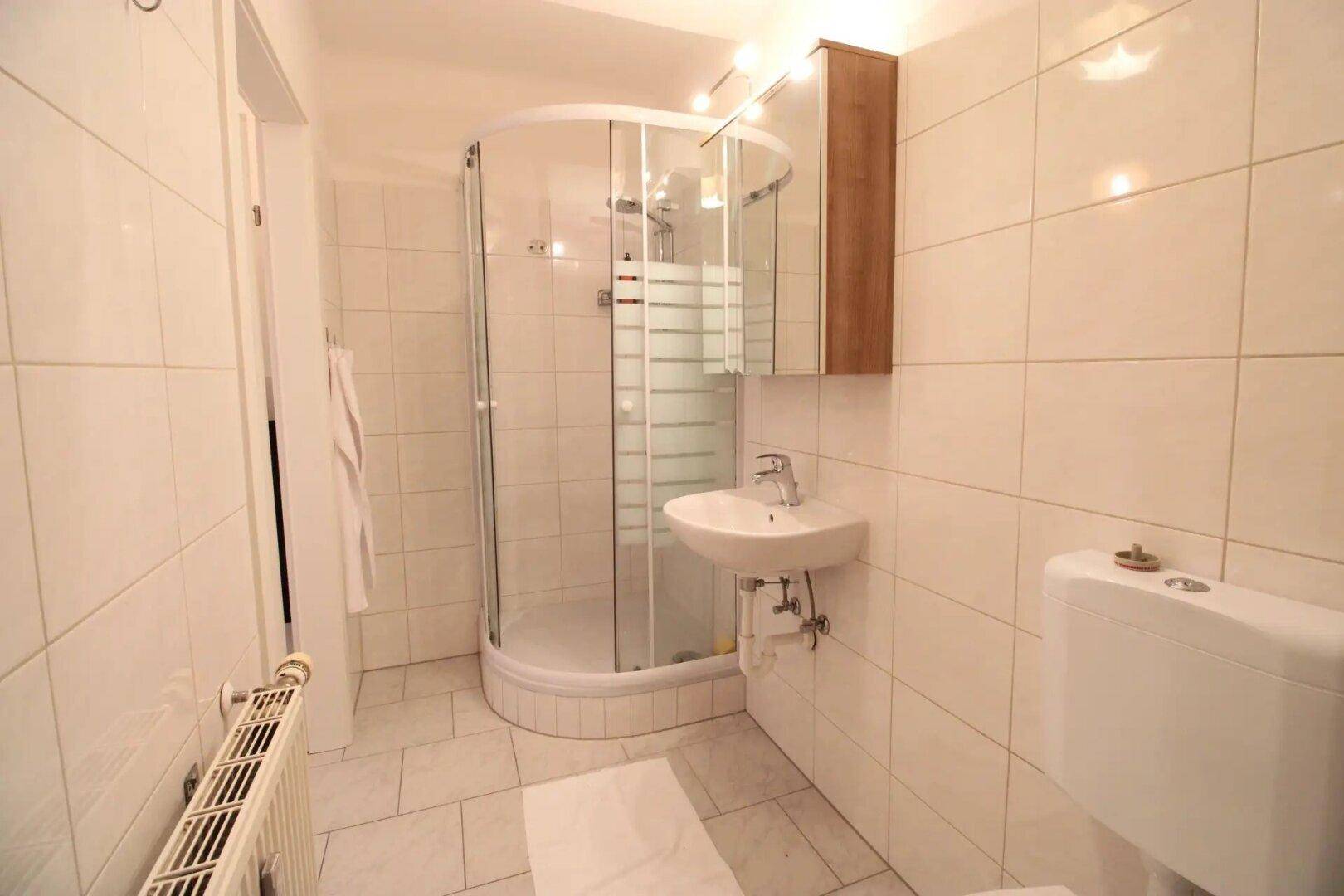 Modernes Badezimmer mit Duschkabine, WC und Waschbecken, komplett mit hellen Fliesen ausgestattet.