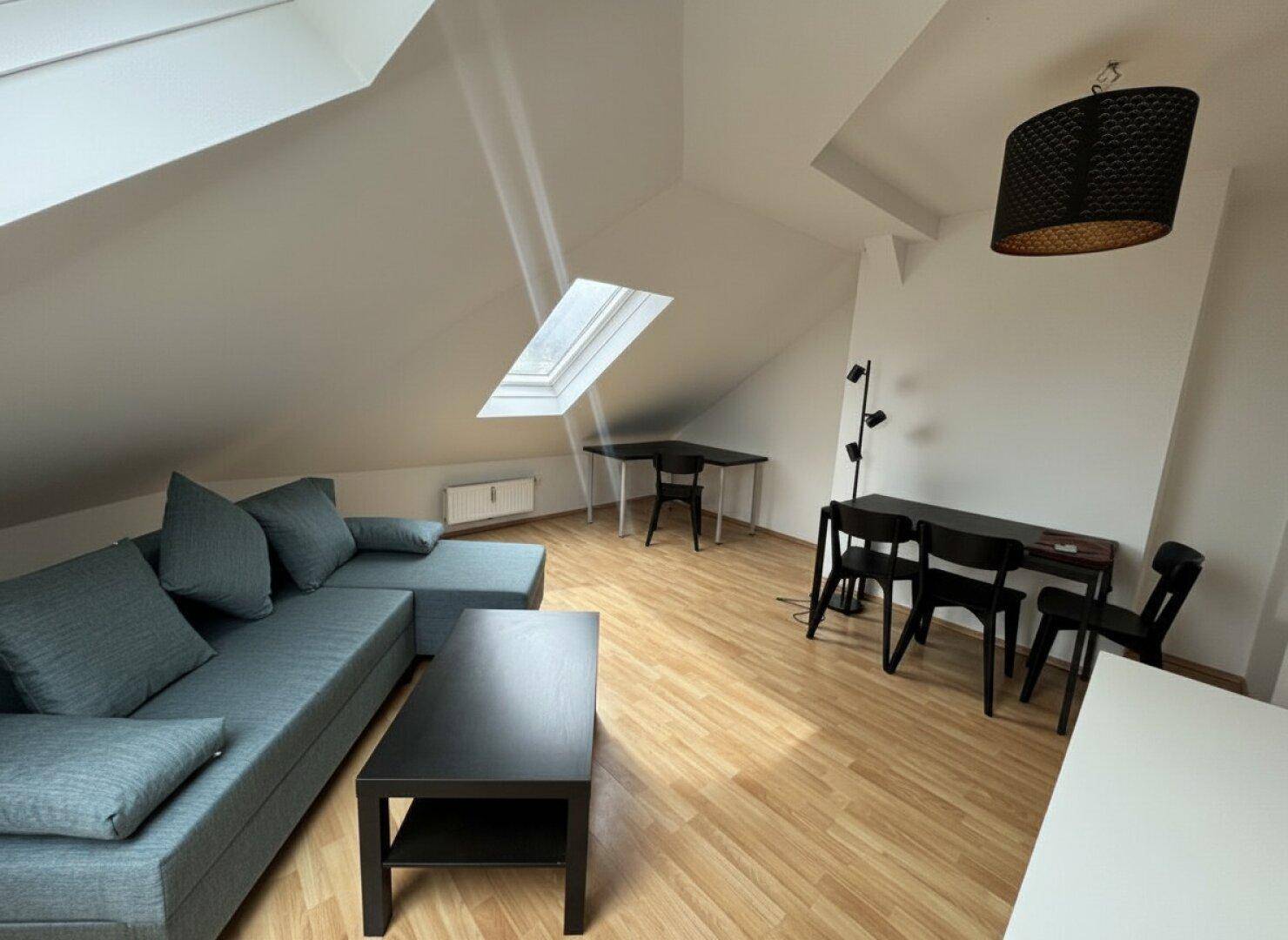 Geräumiger Wohn-Essbereich im Dachgeschoss mit schrägen Wänden und viel Tageslicht durch ein Dachfenster.