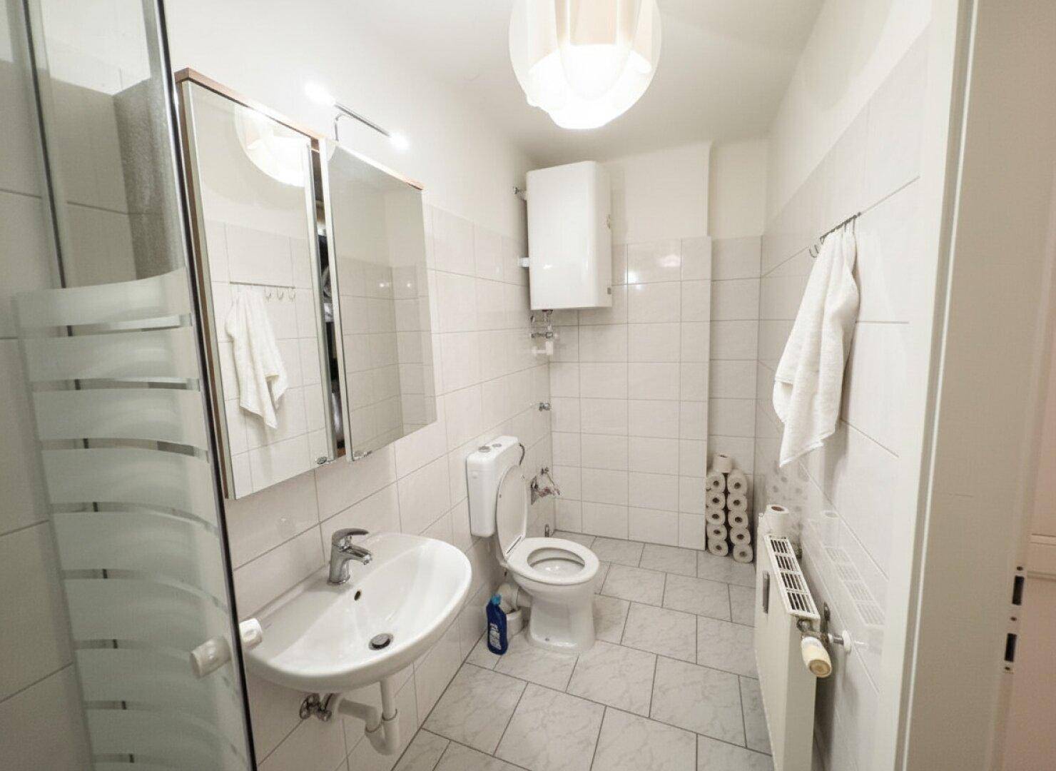 Funktionales Badezimmer mit Duschkabine, WC, Waschbecken und Spiegelschrank über dem Waschtisch.