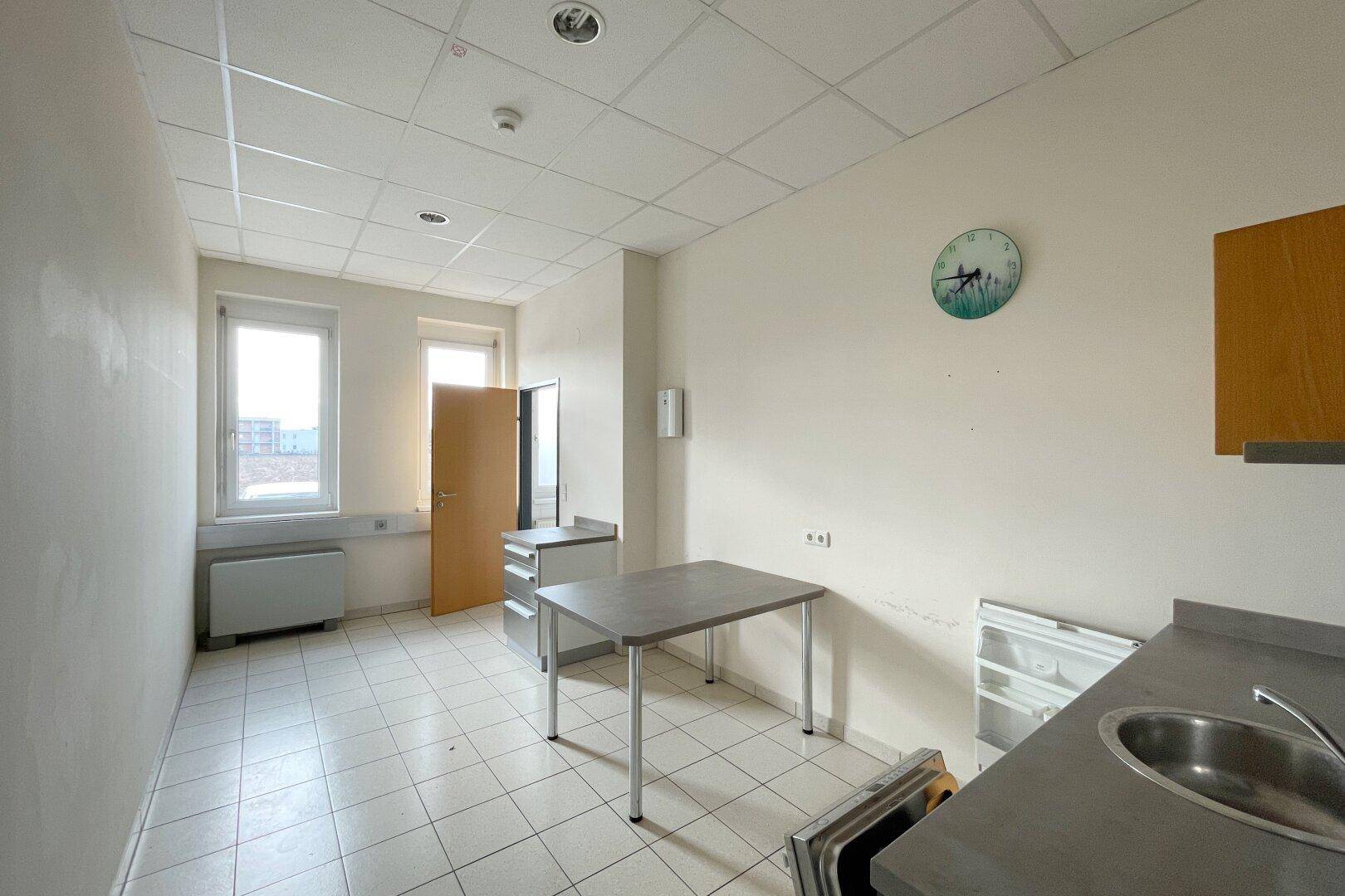Einfache Küchenzeile mit Spüle, Kühlschrank und Tisch, ideal für Pausen in einem Bürogebäude.