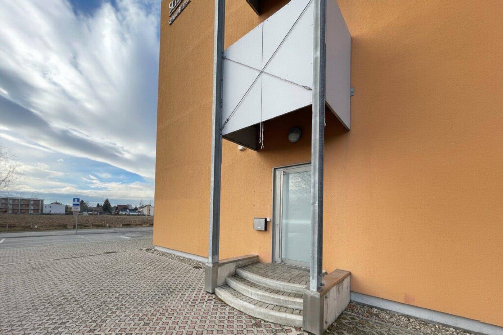 Moderne Gebäudefassade in Orange mit Eingangsbereich und Parkplätzen davor.