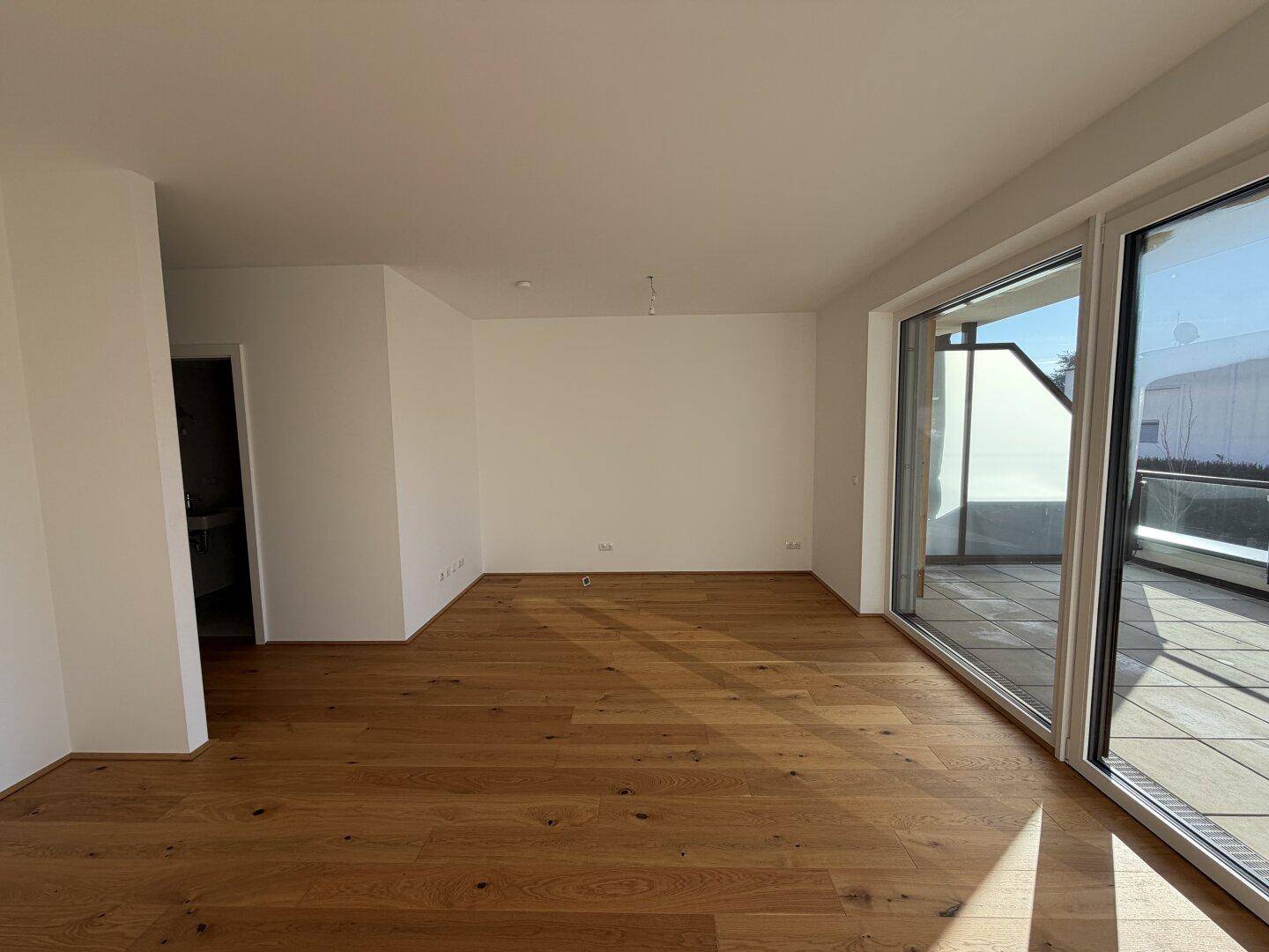 Heller Wohnraum mit Eichenparkettboden und großen Fenstern, die direkten Zugang zum Balkon bieten.