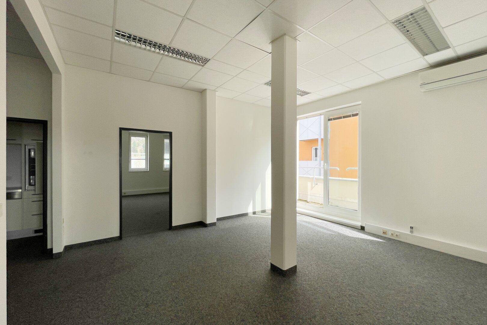Geräumiges Büro mit Teppichboden, weiß gestrichenen Wänden und einem Pfeiler in der Mitte des Raumes.
