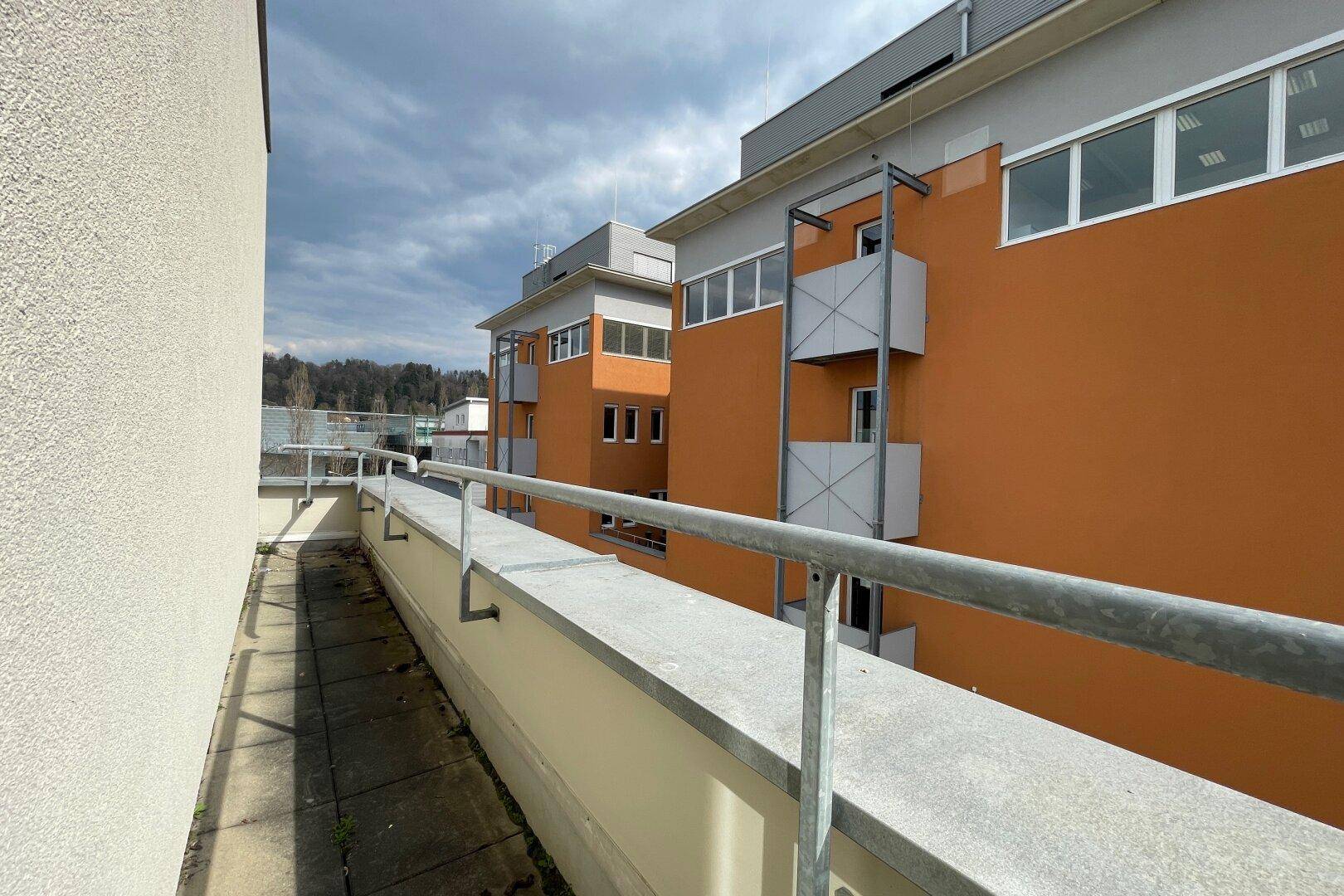 Schmaler Balkon mit Metallgeländer und Blick auf die orangefarbene Fassade des Nachbargebäudes.