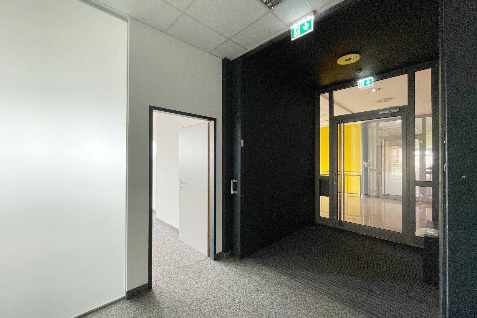 Moderner Flur mit dunklem Teppichboden, weißen und schwarzen Wänden sowie Glastüren am Eingangsbereich.