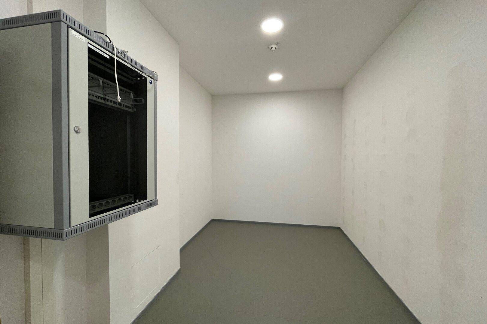 Kleiner Abstellraum mit grauem Boden und einem an der Wand montierten Serverschrank.