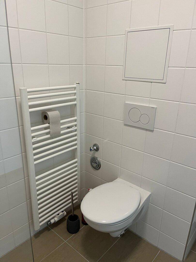 Modernes Badezimmer mit Wand-WC, weißen Fliesen und beheiztem Handtuchhalter.